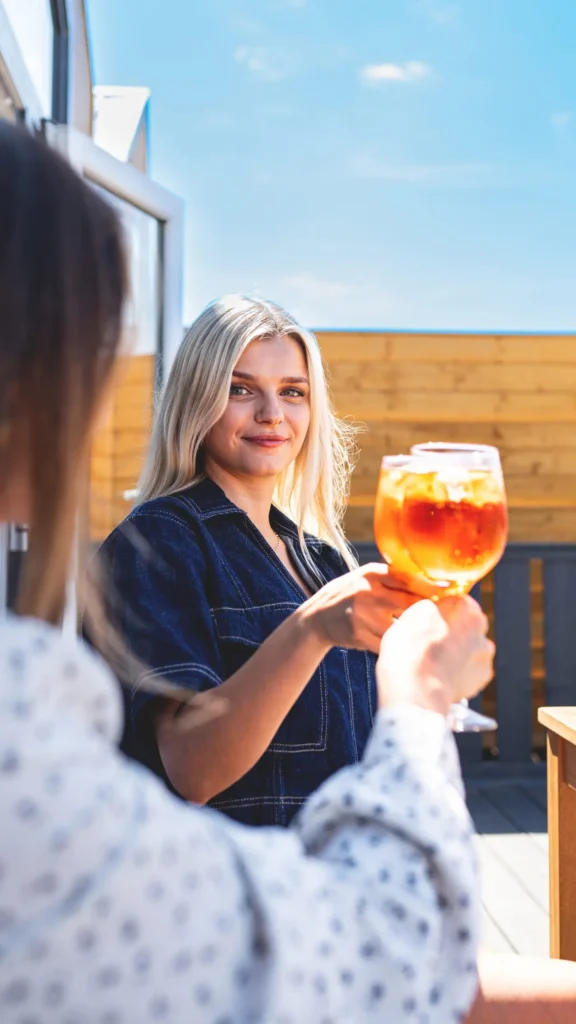 Uśmiechnięte kobiety na tarasie domku stukające się kieliszkami z napojem.
